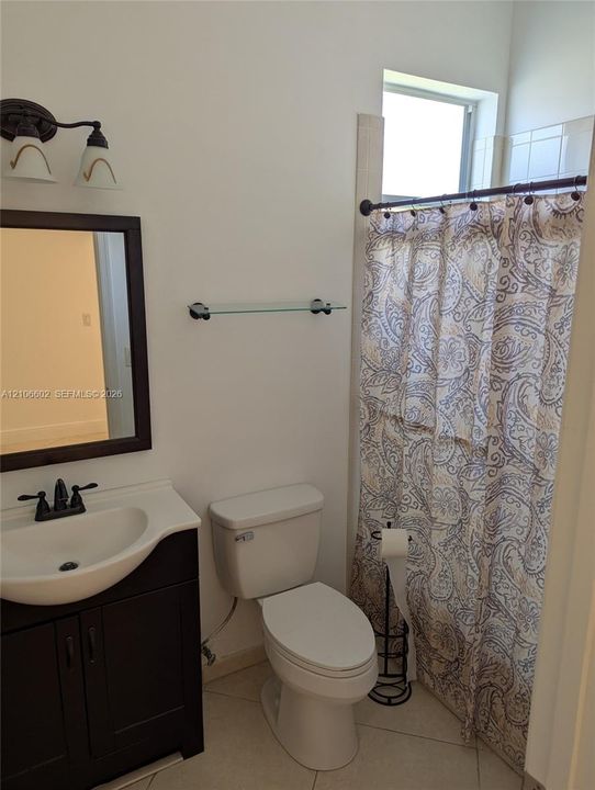 Bathroom featuring a dark-finish vanity with a white integrated basin, dual-handle faucet, framed wall mirror, two-light fixture, and ceramic tile flooring