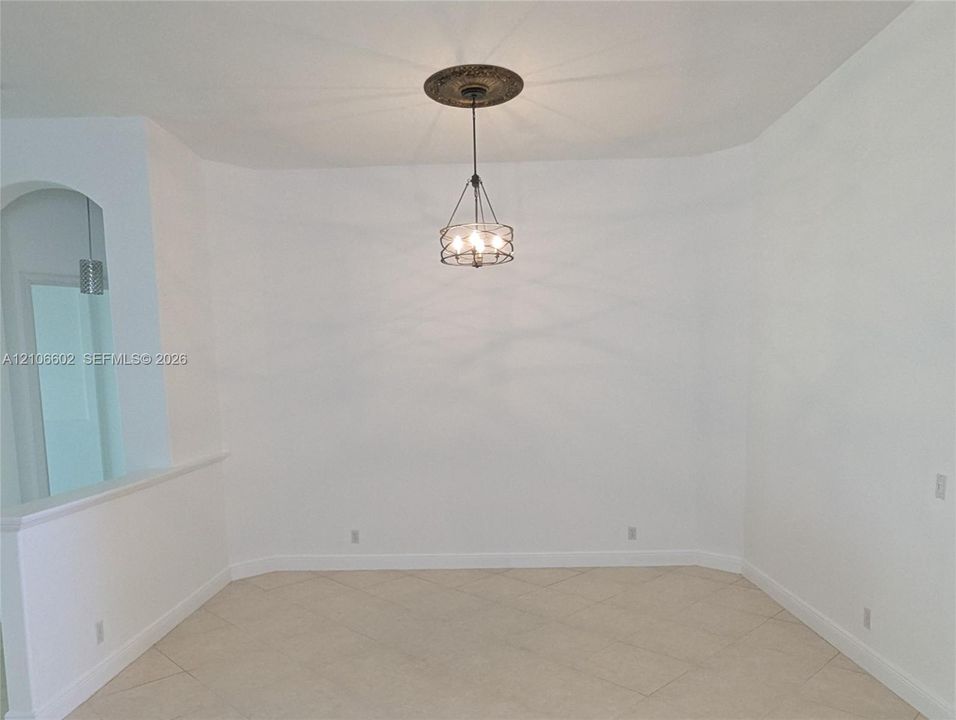 Neutral-toned tile flooring, decorative ceiling medallion, multi-bulb pendant fixture with metal cage frame, and an arched entryway