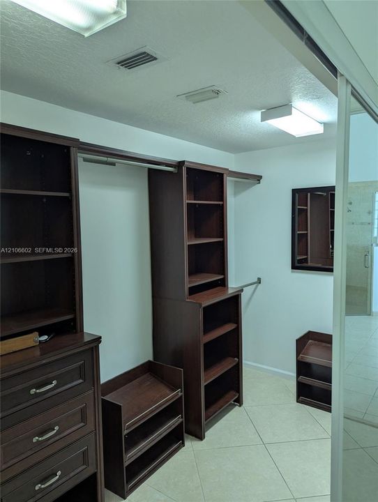 Walk-in closet featuring dark wood-finish built-in cabinetry, integrated shelving units, multi-tier hanging rods, and light-tone tile flooring