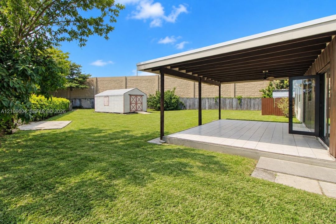 Backyard featuring a covered patio with tile flooring, an expansive lawn, a standalone storage shed, and masonry perimeter wall
