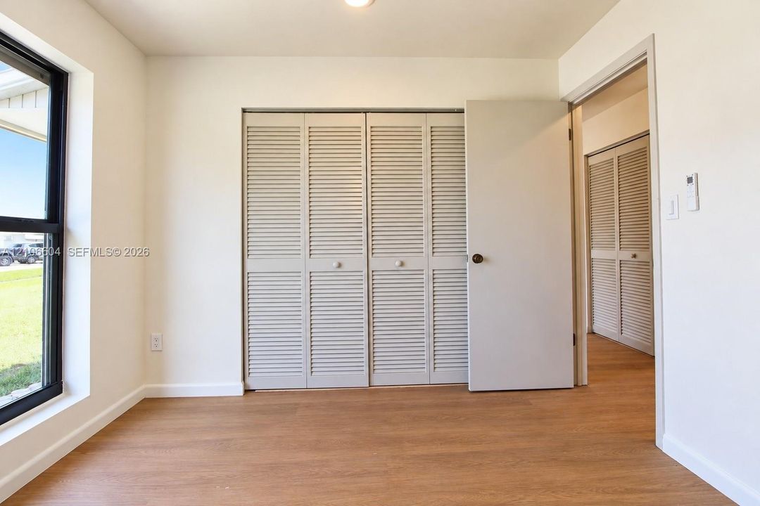 Wood-finish flooring, louvered bi-fold closet doors, a single-panel interior door, and a large window with a black frame
