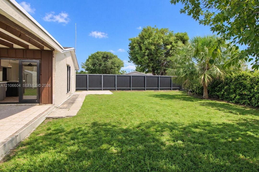 Backyard featuring a paved patio, expansive lawn, mature palm tree, and a privacy fence
