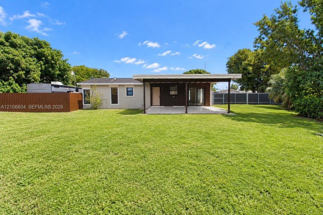 Expansive backyard featuring a manicured lawn, covered patio, privacy fencing, and mature trees