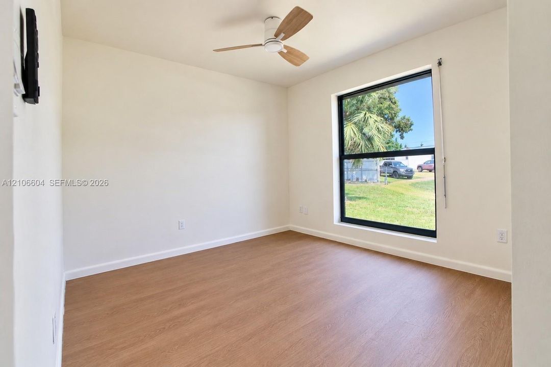 Room featuring wood-finish flooring, a large window with black framing, and a ceiling fan with light-toned blades