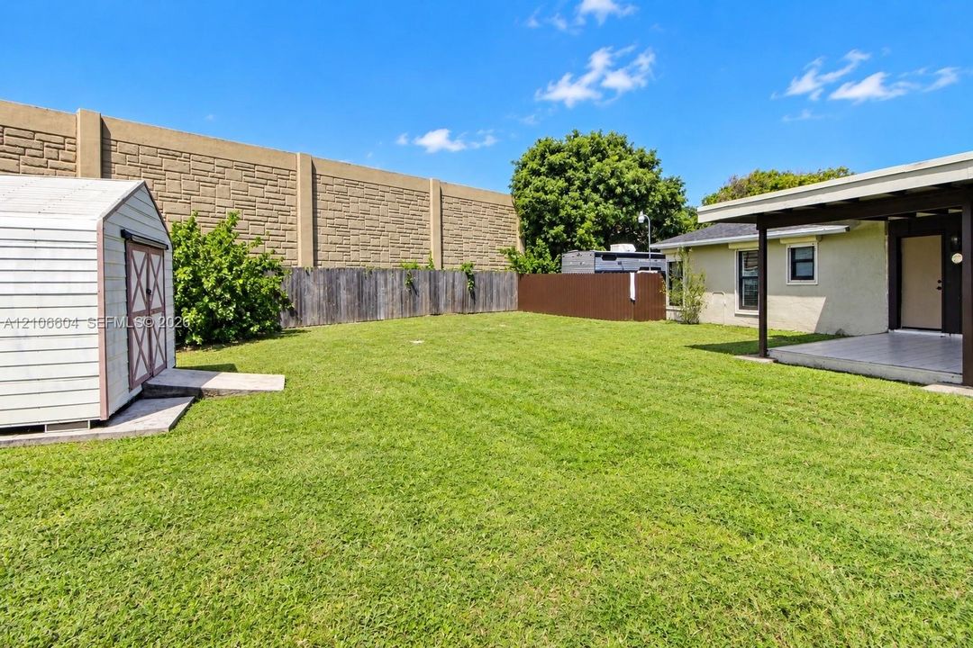 Backyard featuring a grass lawn, covered patio, detached storage structure, concrete masonry perimeter wall, and wood privacy fencing