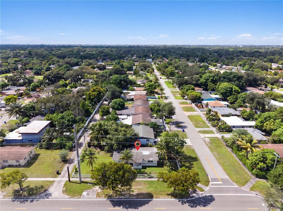 Aerial perspective of a corner lot property featuring established landscaping, mature palm trees, a concrete driveway, and a residential structure with a shingled roof