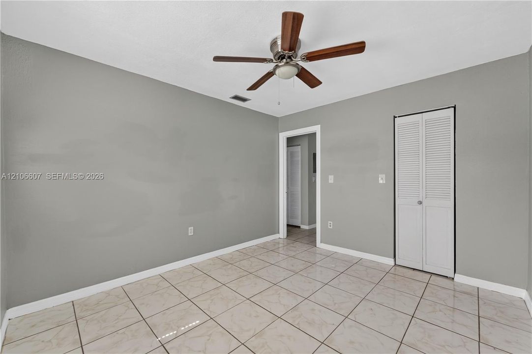 Neutral-toned interior featuring square tile flooring, a ceiling fan with integrated lighting, and a bi-fold louvered closet door