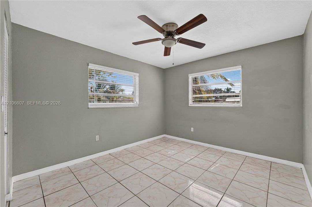 Neutral-toned interior space featuring ceramic tile flooring, horizontal slat window blinds, and a central ceiling fan with integrated light fixture