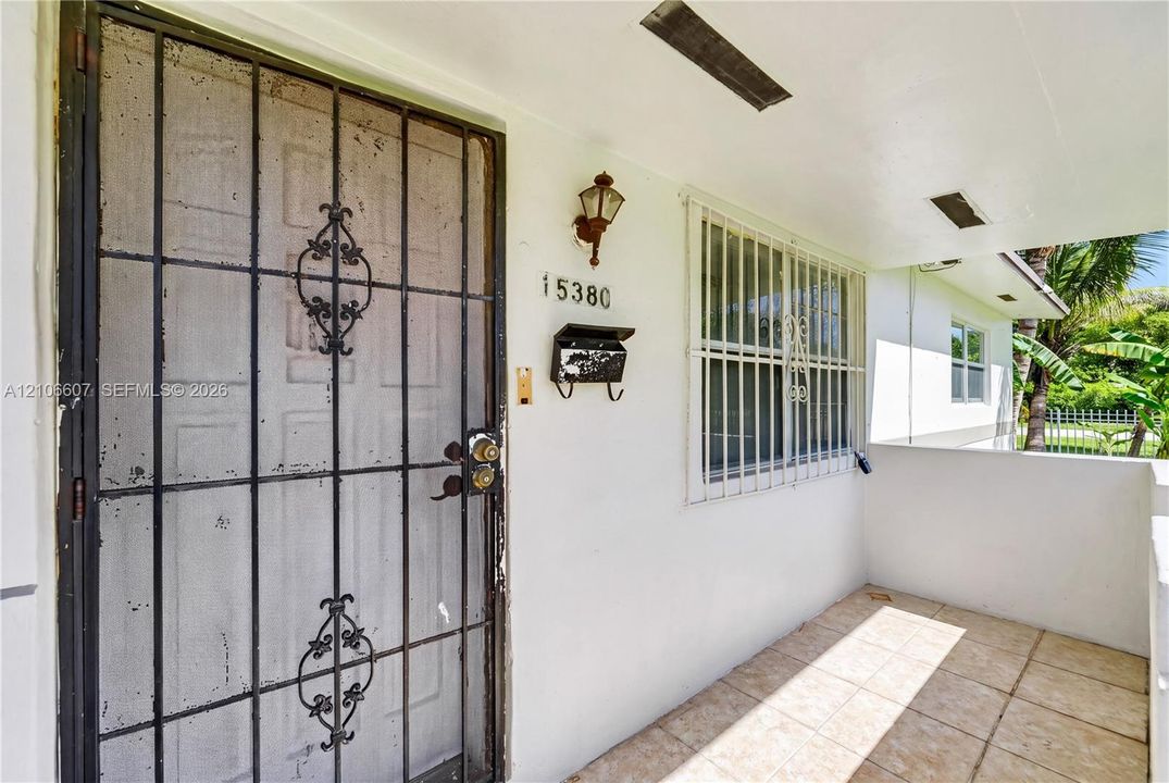 Covered entryway featuring light-toned tile flooring, metal security door, metal window security bars, and wall-mounted exterior lighting