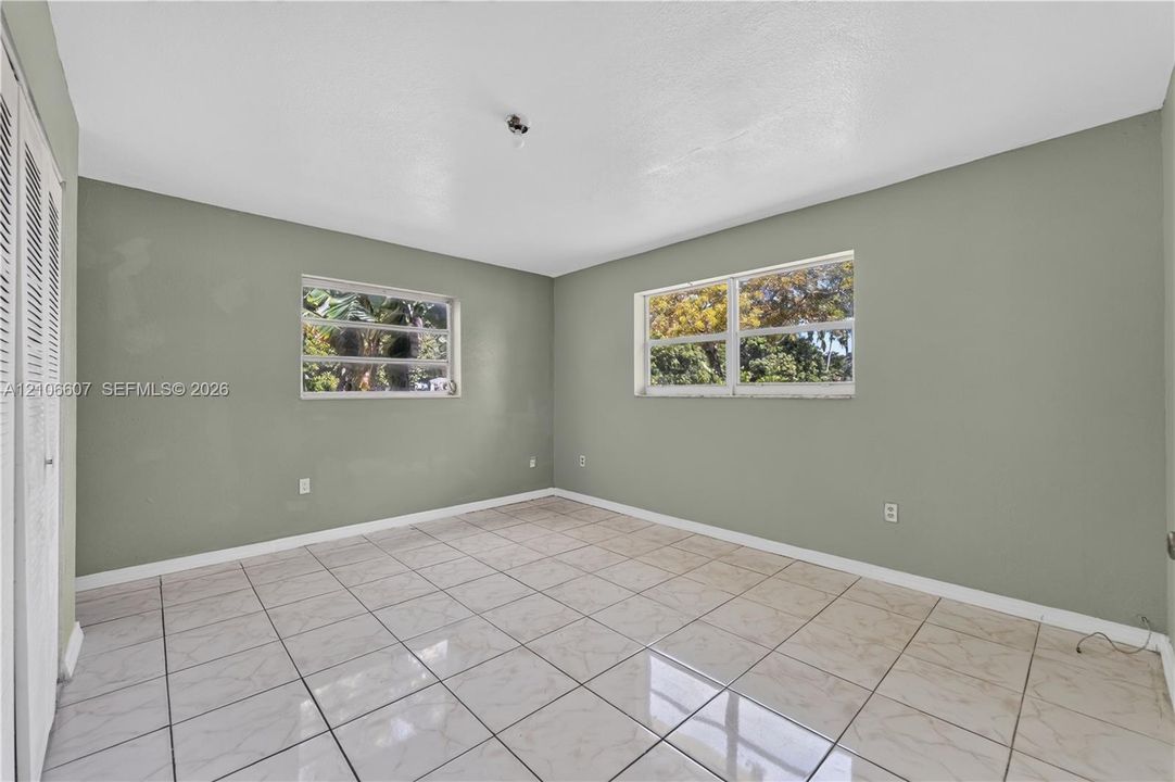 Interior room featuring neutral-toned walls, tile flooring, two horizontal sliding windows, and a set of double louvered closet doors