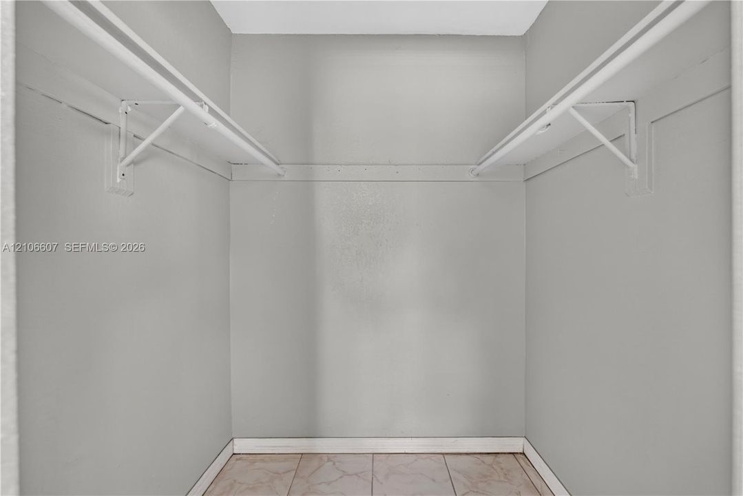 Walk-in closet featuring dual-level white shelving and tile flooring