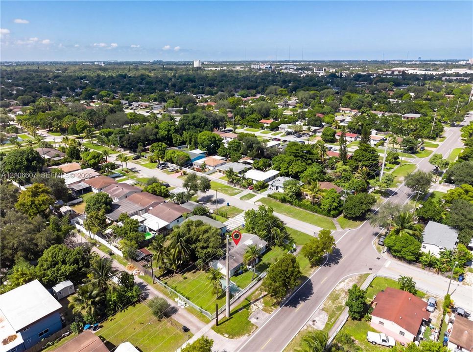Aerial perspective of a corner lot property featuring a single-story residence, expansive green space, mature palm trees, and perimeter fencing