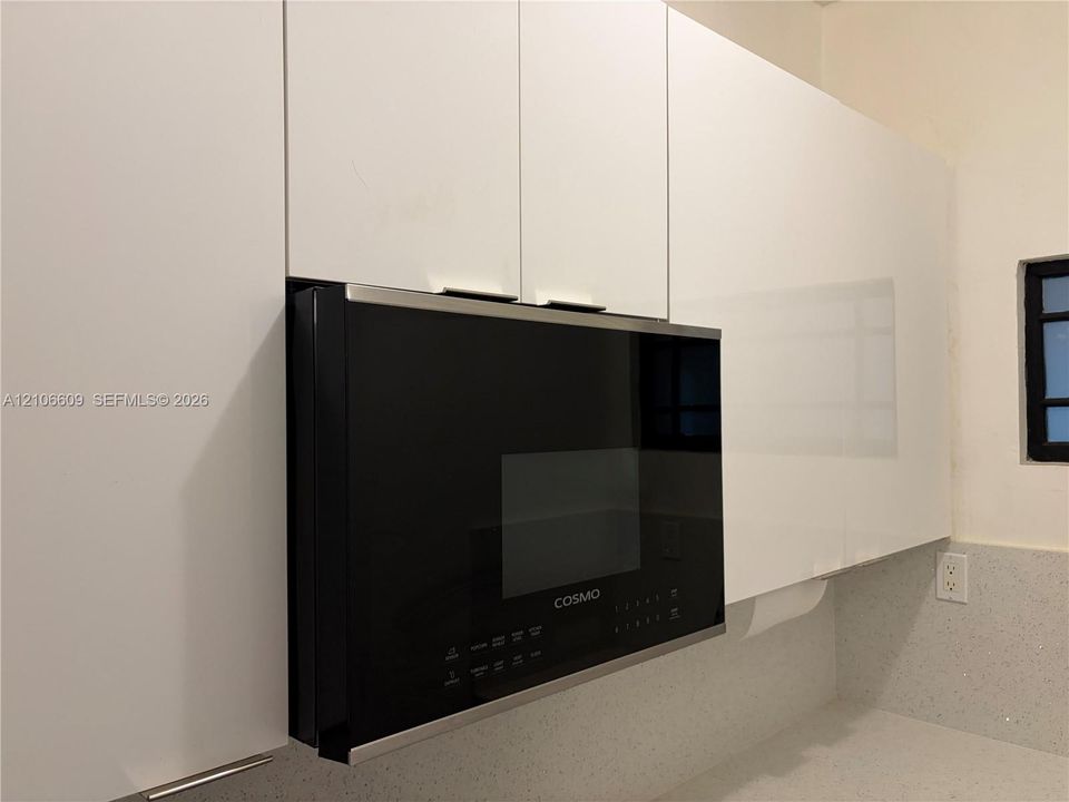 Sleek white flat-panel cabinetry, integrated black microwave, quartz countertop, and grid-pattern window