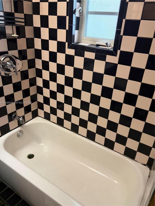 Standard-sized bathtub with a polished chrome faucet and shower handle, featuring a high-contrast black and white checkered tile surround