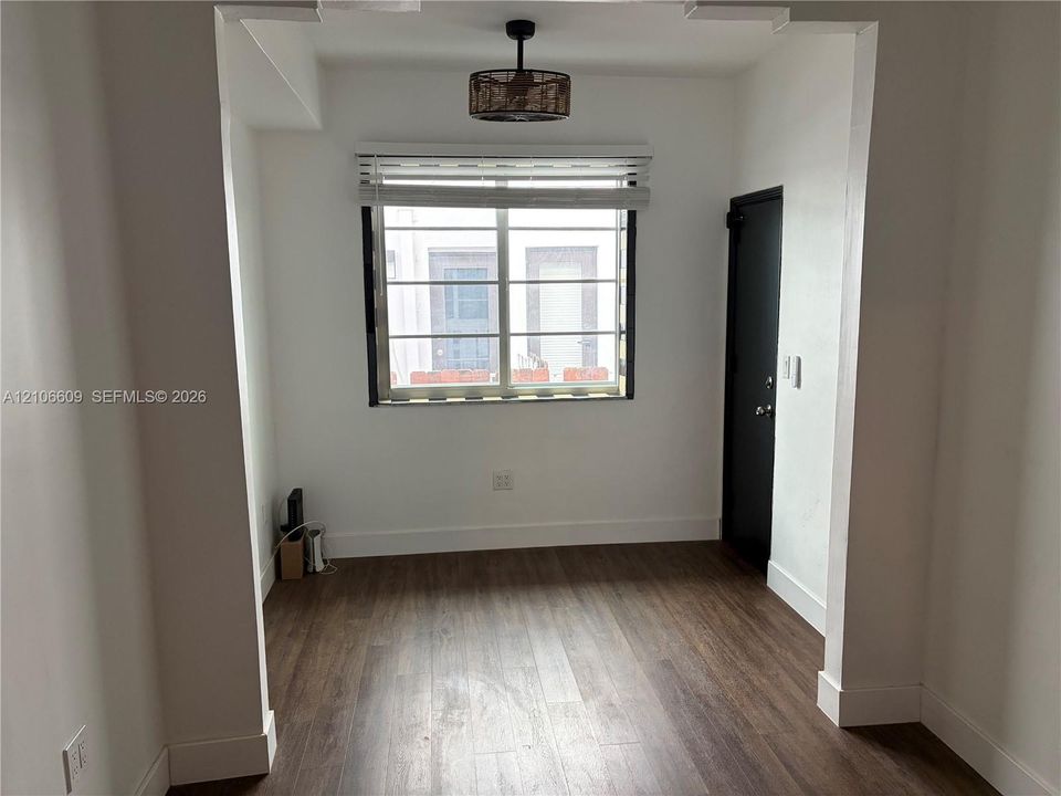 Room featuring wood-finish flooring, a drum-style ceiling light fixture, a single-hung window with horizontal blinds, and a solid-panel door with dark hardware