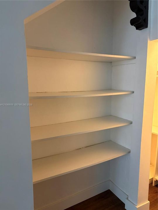 Built-in alcove featuring four recessed white shelving units and wood-finish flooring