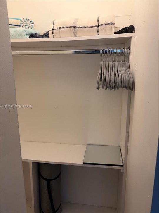 Built-in storage closet featuring tiered shelving and a polished metal garment rod