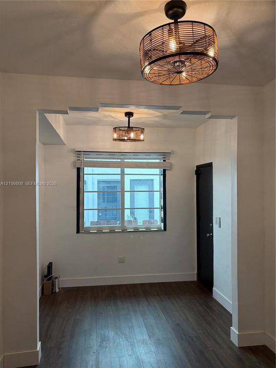 Interior space featuring wood-finish flooring, dual decorative metal-mesh drum light fixtures, a single-hung window with horizontal blinds, and a solid-core door with matte black hardware