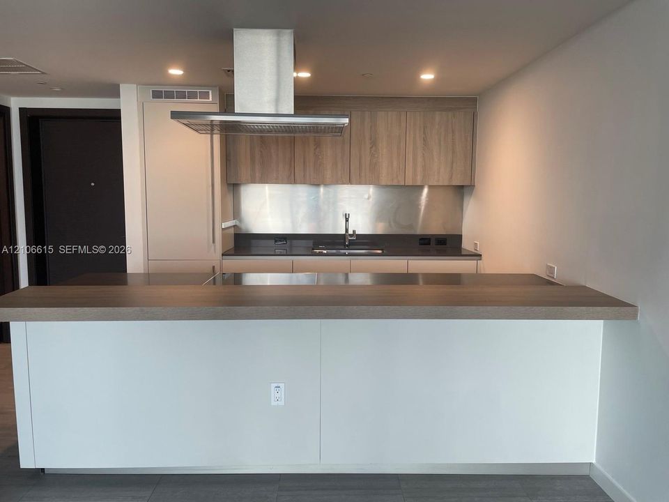 Kitchen featuring a wood-finish island with a countertop, stainless steel range hood, full-height wood-finish cabinetry, a metal backsplash, and recessed lighting