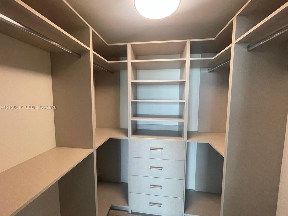 Walk-in closet featuring custom built-in shelving, four integrated drawers, overhead lighting, and dual hanging rods