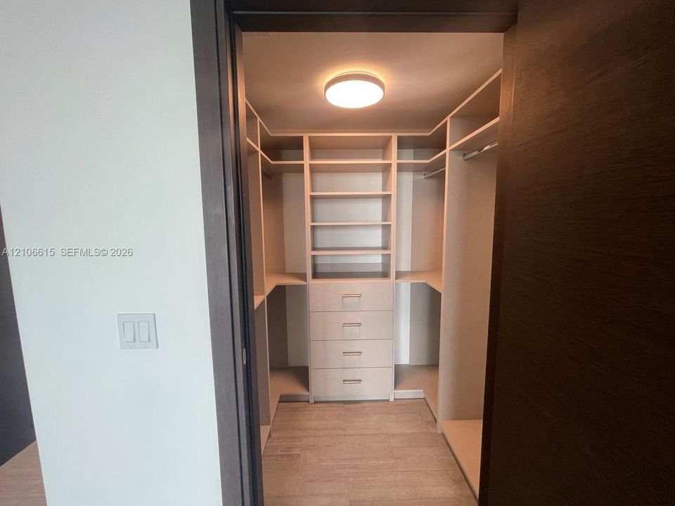 Walk-in closet featuring custom light-finish built-in cabinetry, floor-to-ceiling shelving, integrated storage drawers, and ceiling-mounted flush light fixture