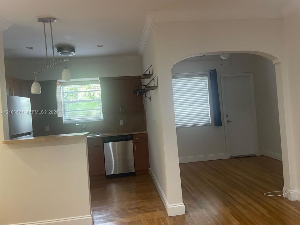 Kitchen featuring wood cabinetry, stainless steel appliances, a peninsula counter, and pendant lighting, opening through an arched entryway to hardwood flooring