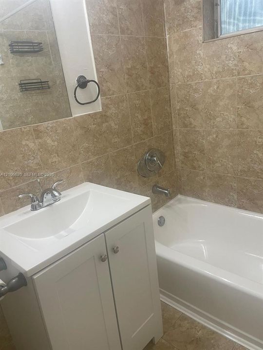 White shaker-style vanity with a composite countertop and integrated basin, complemented by tile wall surround, tub-shower combination, and polished chrome fixtures