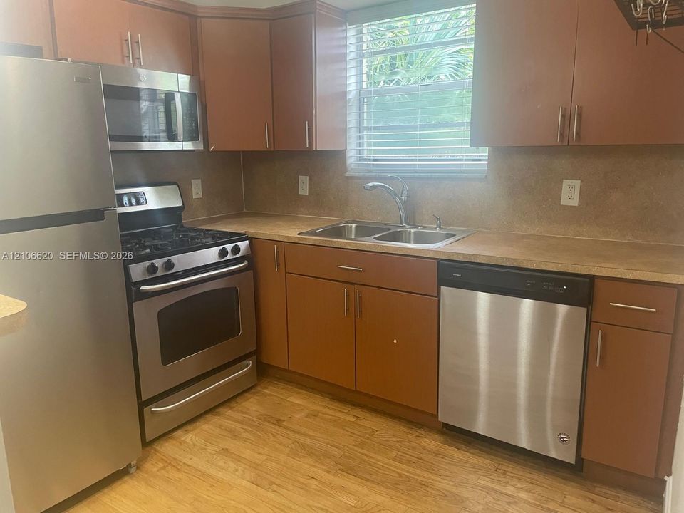Kitchen featuring wood-finish cabinetry, stainless steel appliances, double-basin sink with pull-down faucet, solid-surface countertops, and wood-finish flooring