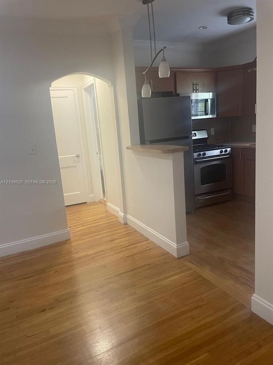 Kitchen featuring wood-finish cabinetry, stainless steel appliances, and a breakfast bar, complemented by wood-finish flooring and an arched entryway