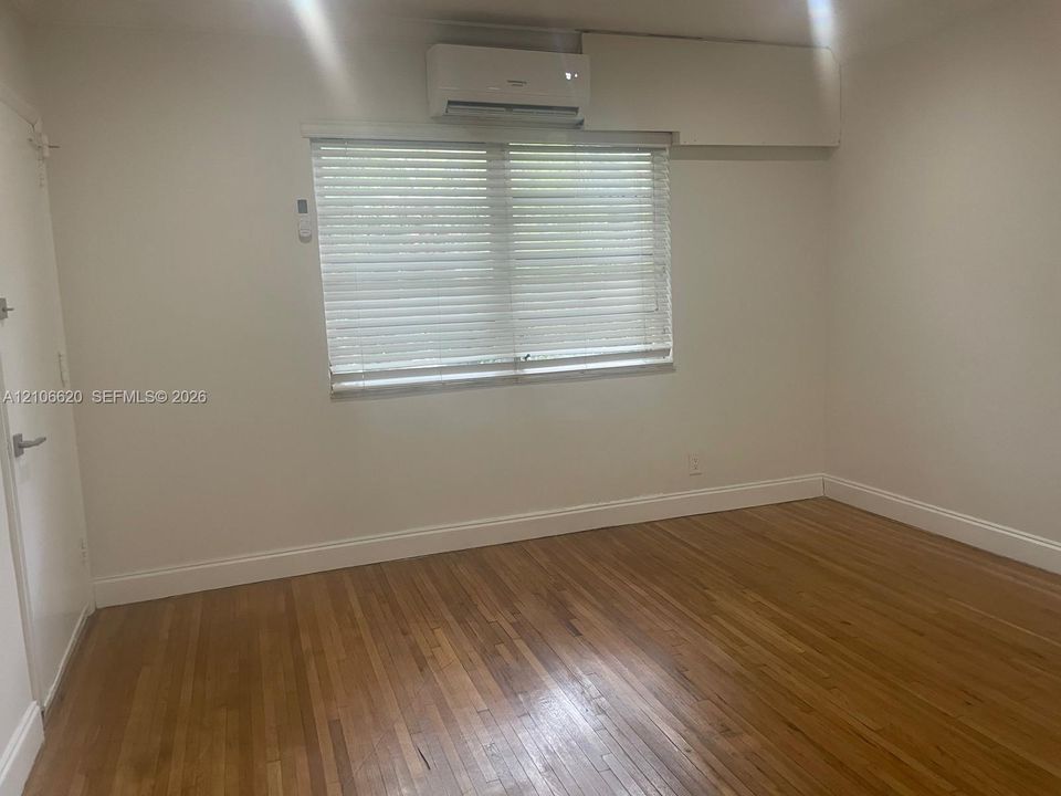 Interior room featuring wood-finish flooring, a wall-mounted ductless mini-split air conditioning unit, and a window with horizontal blinds