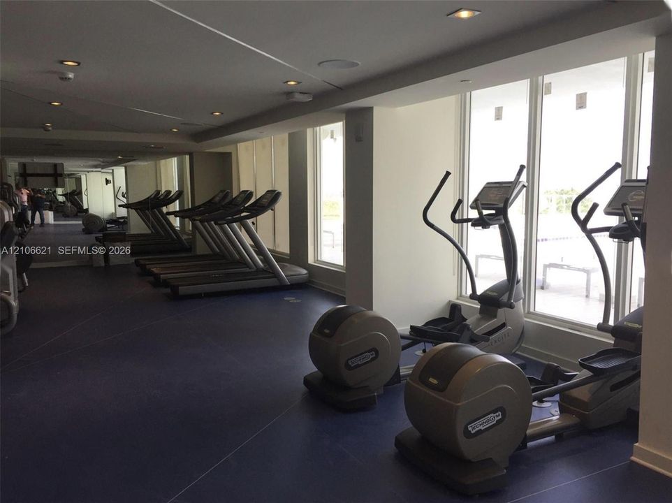 Fitness center featuring floor-to-ceiling windows, recessed lighting, mirrored walls, and dark rubberized flooring