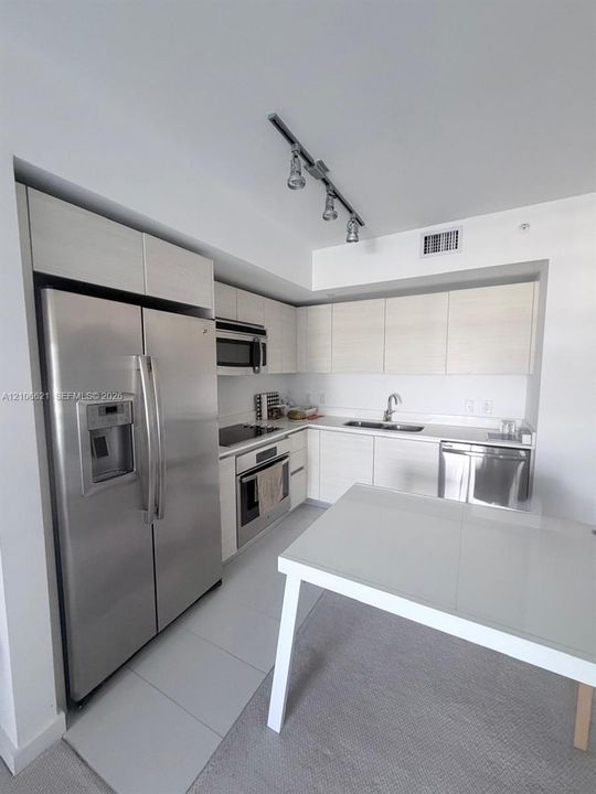 Kitchen featuring flat-panel cabinetry, stainless steel appliances, track lighting, dual-basin sink, and solid-surface countertops
