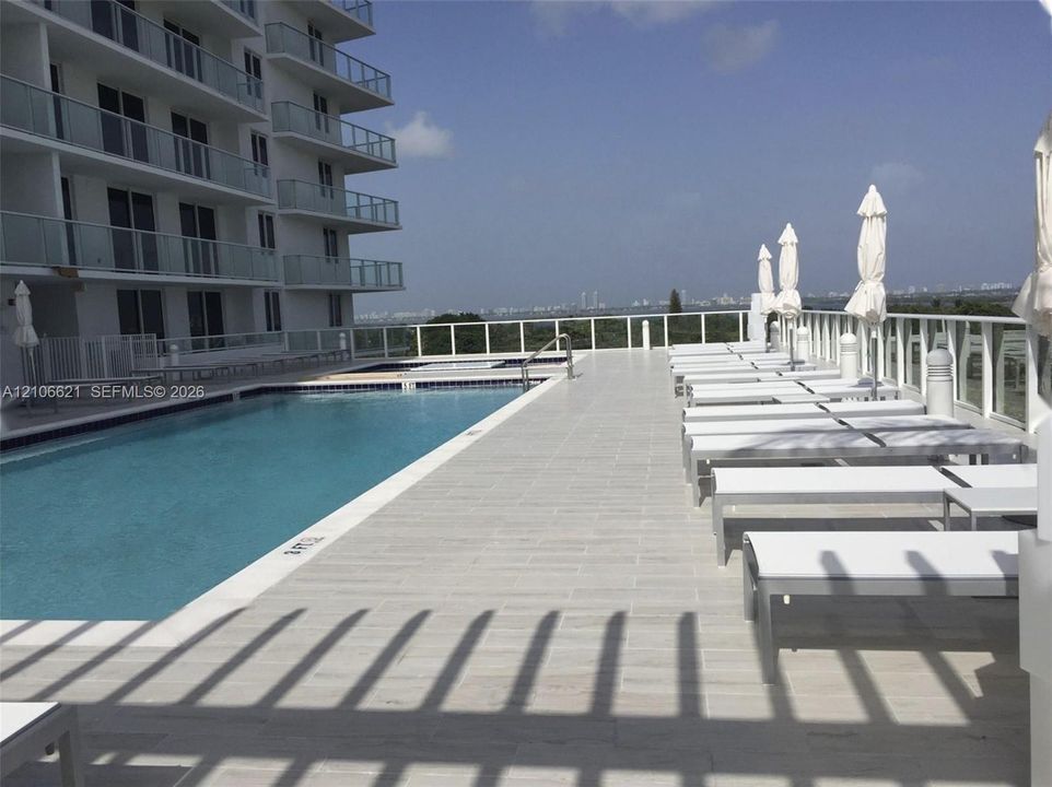 Swimming pool featuring light-toned paved decking and a glass-paneled perimeter railing