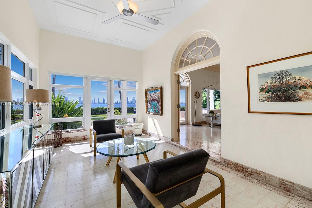 Sunroom featuring geometric coffered ceilings, stone-tile flooring, large-format windows, and an arched entry with a decorative fanlight