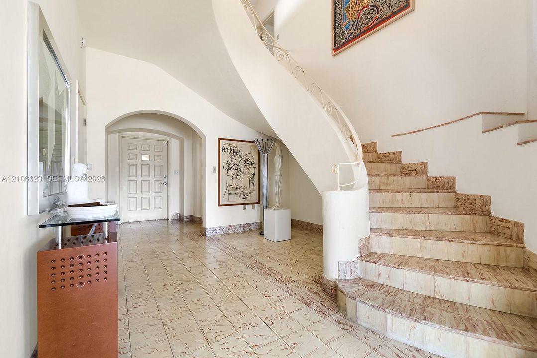 Curved staircase featuring custom metal railings and stone steps, complemented by stone-tile flooring and an arched entryway
