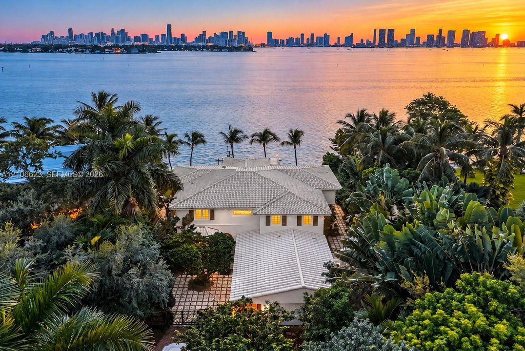 Waterfront estate featuring a tile roof, paved courtyard, lush landscaping, and a direct city skyline backdrop