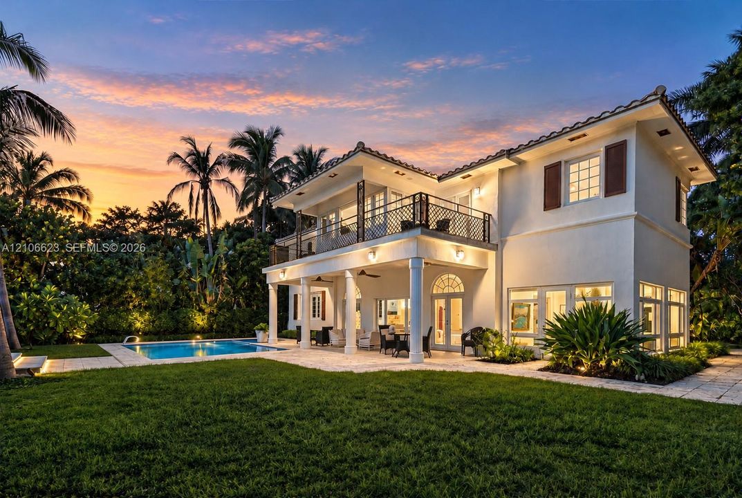Two-story exterior featuring a light-toned facade, second-story balcony with decorative metal railing, covered ground-level loggia supported by classical columns, and an inground swimming pool set within a paved patio area