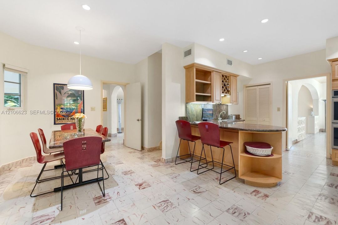 Kitchen featuring light wood cabinetry, stone countertops, a peninsula with integrated shelving, and stone tile flooring