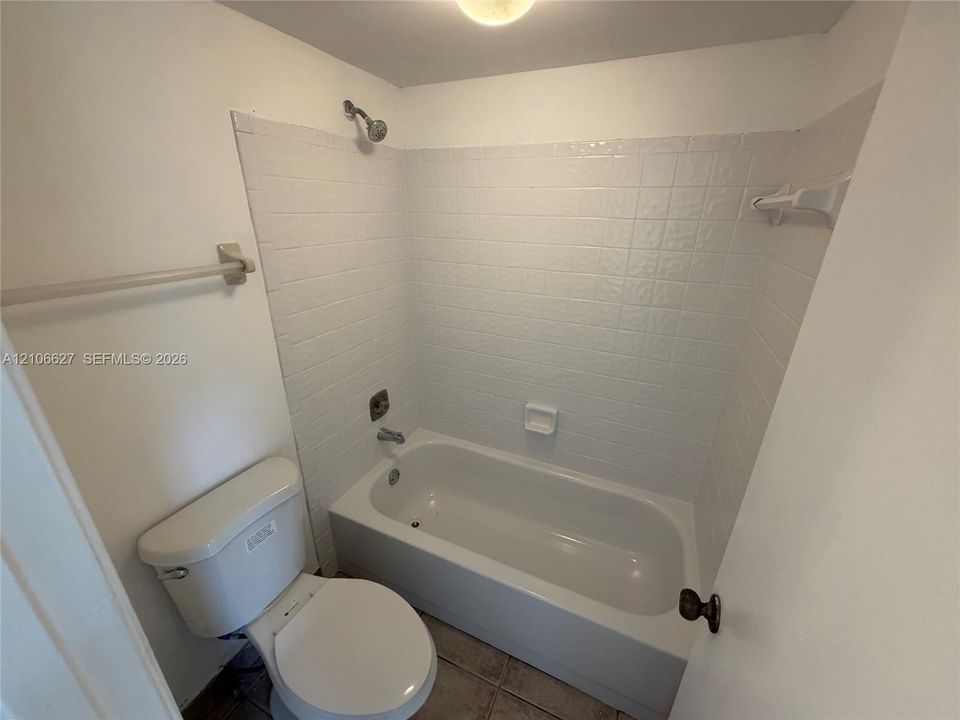 Bathtub and shower combination with white square tile surround, ceramic tile flooring, chrome hardware, and white toilet