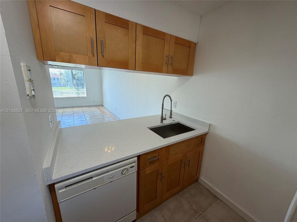 Kitchen area featuring wood cabinetry, solid-surface countertop with integrated backsplash, undermount sink with gooseneck faucet, and white dishwasher