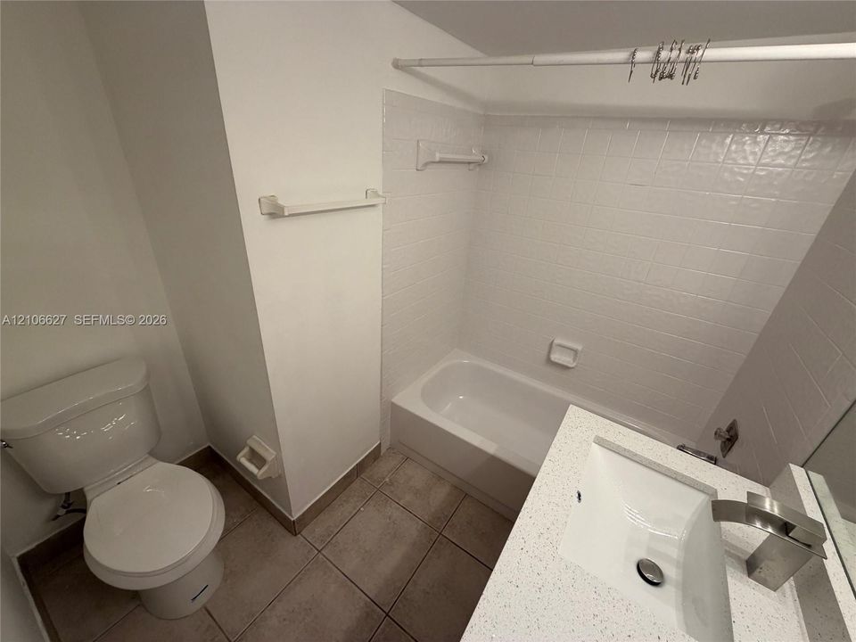 Bathroom featuring a vanity with a rectangular sink, stone-composite countertop, and a brushed-metal faucet, accompanied by a tiled tub enclosure and large-format floor tile