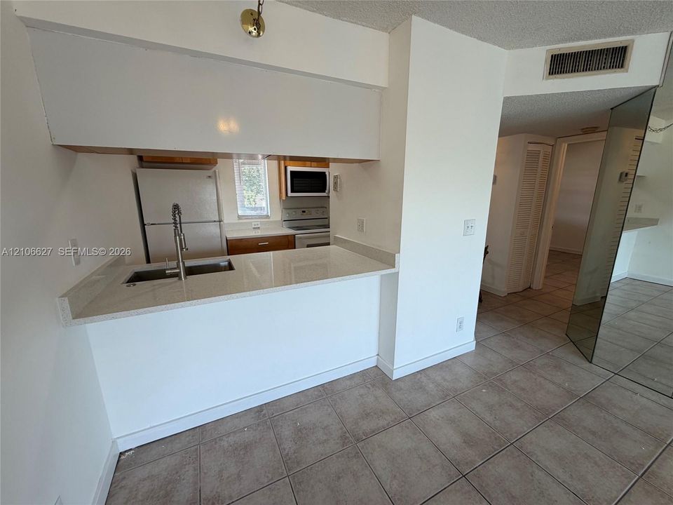 Kitchen featuring a peninsula with a composite countertop, an undermount stainless steel sink, a gooseneck faucet, tile flooring, and mirrored paneling