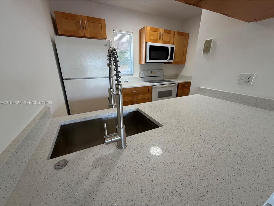 Kitchen featuring light-toned cabinetry, solid surface countertops, a stainless steel undermount sink, a gooseneck faucet, and built-in appliances