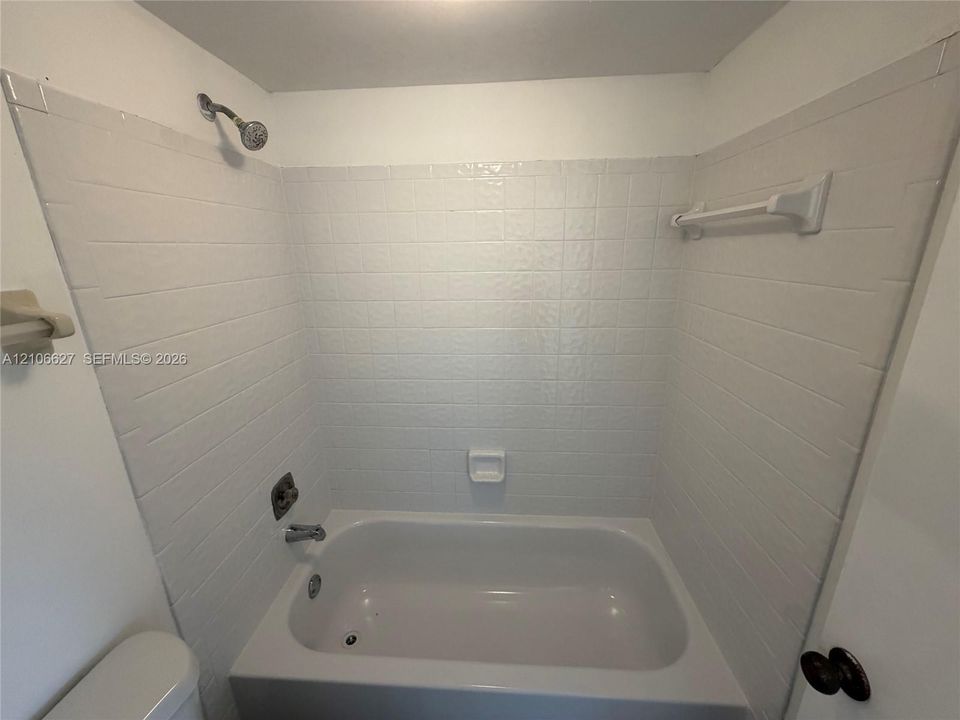 Tub and shower combination featuring a white tile surround, integrated soap dish, chrome shower head, and wall-mounted towel bar