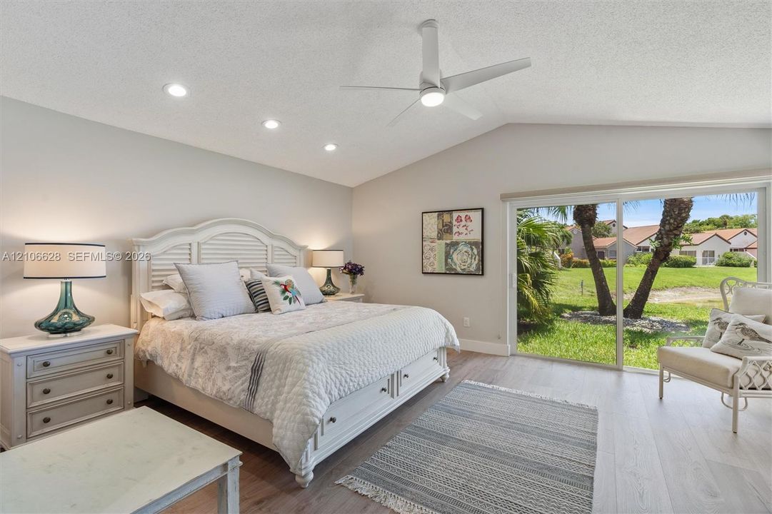 Vaulted ceiling with recessed lighting and a central ceiling fan, wood-finish flooring, and sliding glass doors with exterior landscaping