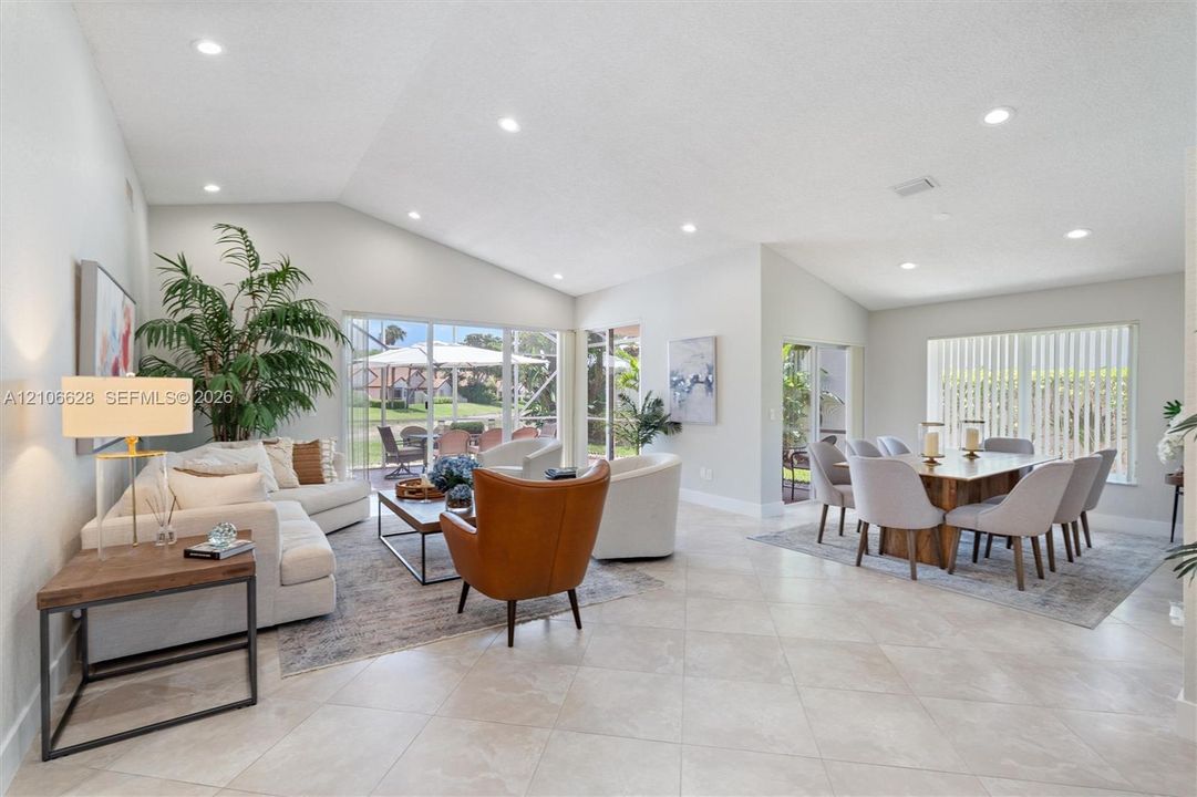 Vaulted ceilings, neutral tile flooring, recessed lighting, and large sliding glass doors providing outdoor access