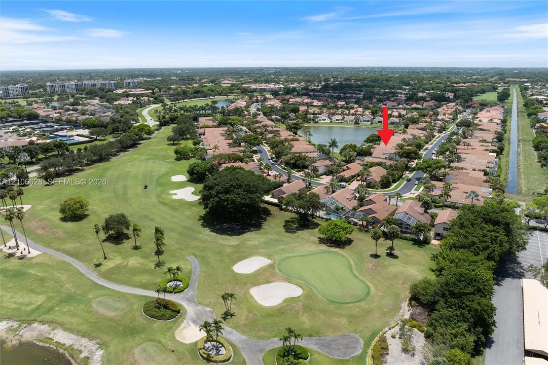 Aerial perspective of a residential property featuring proximity to an expansive golf course, mature landscaping, and a nearby lake