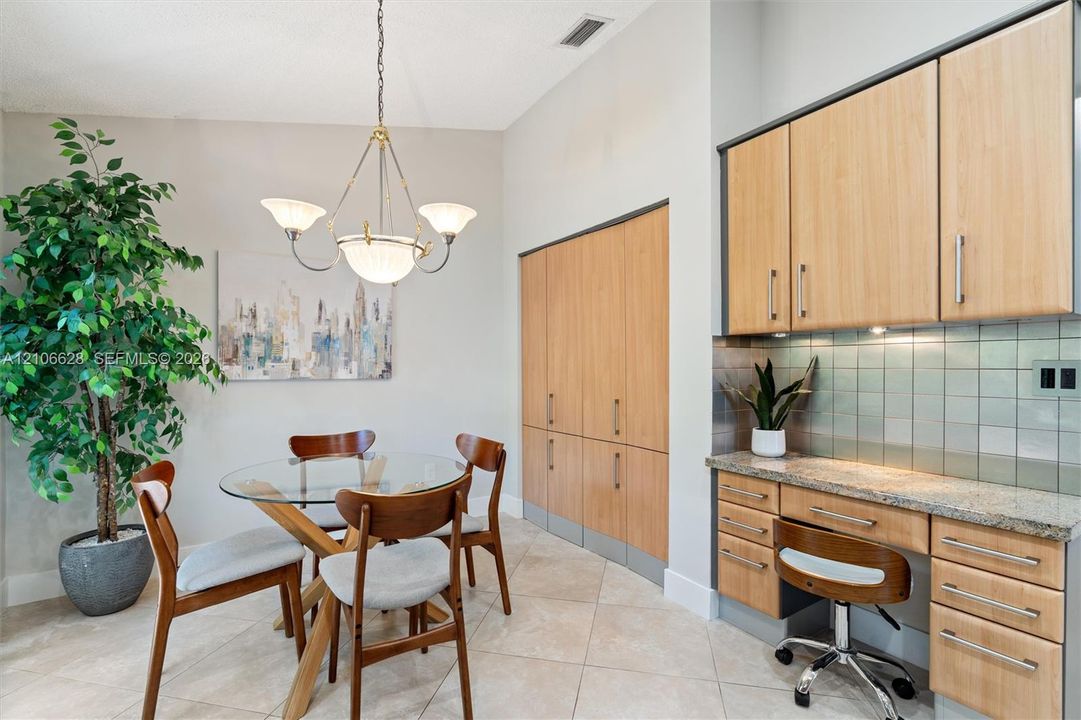 Built-in light-tone cabinetry, stone countertop workspace, tiled backsplash, and decorative multi-arm chandelier