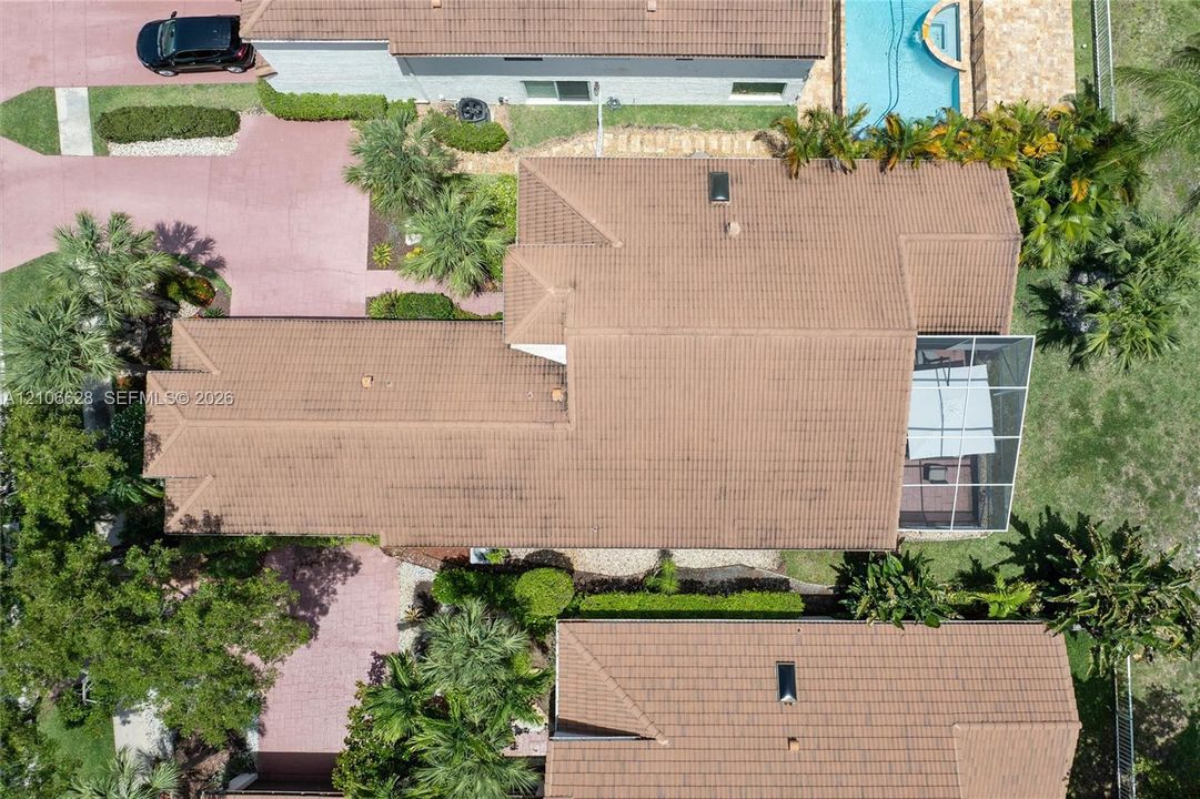 Aerial perspective featuring a tile roof, an in-ground pool with stone-finish decking, and a screened-in lanai