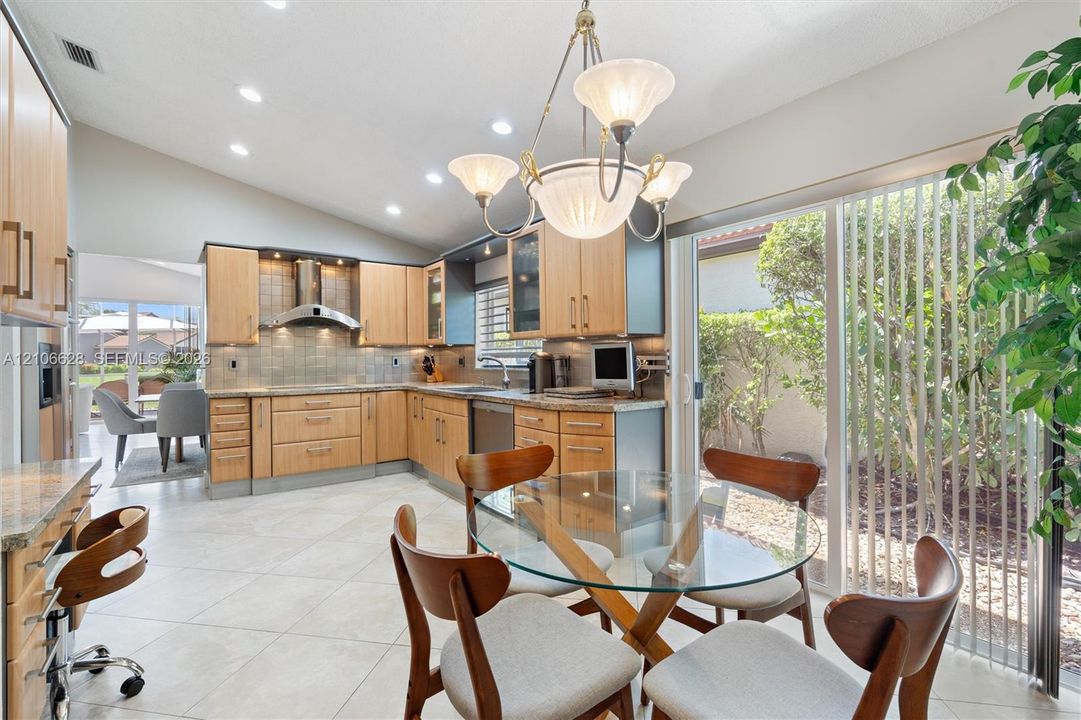 Kitchen featuring wood cabinetry, stone countertops, stainless steel range hood, recessed lighting, and large sliding glass doors